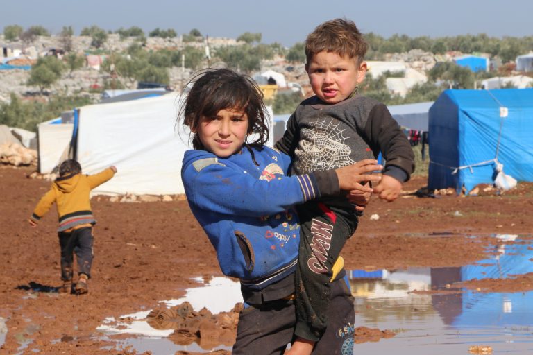 Syrian girls poses for the camera as she holds her younger sibling at a refugee camp during winter.