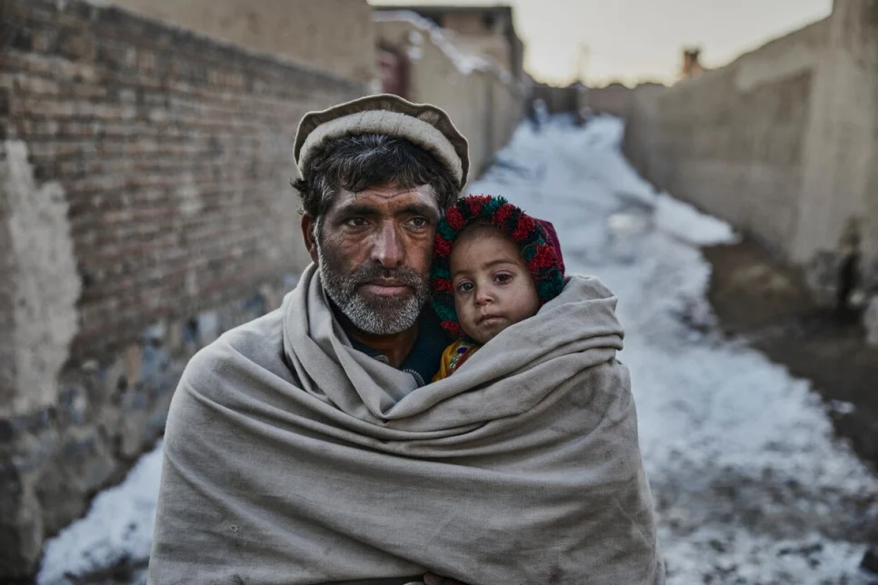 A Pakistani man wraps himself and his daughter inside of his shawl during the cold winter months.