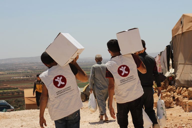 HCI workers are seen walking off into the distance, carrying aid parcels.