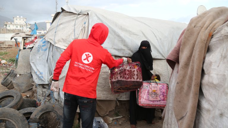 HCI Aid Worker hands out a winter pack to a Yemeni woman, including blankets.